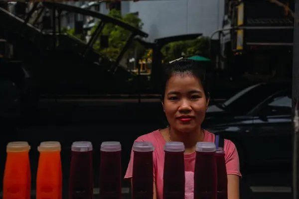 Bangkok, Tayland; 4 Ekim 2024: Tai kadını sakin bir ifadeyle, plastik şişelerde taze nar ve portakal suyu satıyor, Sukhumvit yolunda, Camara 'ya bakıyor