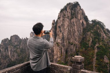 Sonbaharın bulutlu bir gününde Çin 'in Huangshan kentindeki Sarı Dağ' da telefonuyla dramatik bir dağ fotoğrafı çeken adamın arka planı.