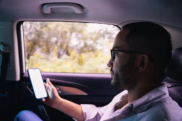 İş adamı takside telefonunu taksici kıyafeti ve gözlükleriyle kullanıyor.