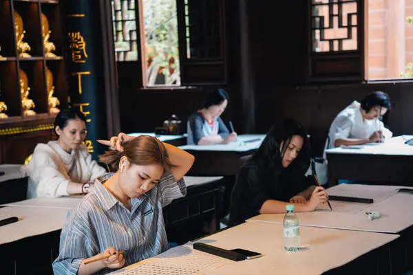 Şangay, Çin; 15 Ekim 2024: Çin 'deki Jade Buddha Tapınağı' nda geleneksel Çince kaligrafi öğrenen ve pratik yapan bir grup kadın