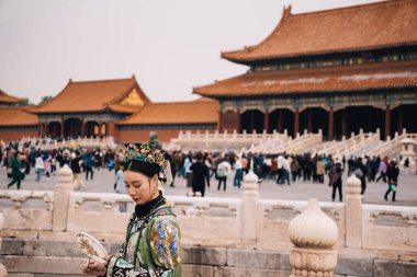 Pekin, Çin; 17 Ekim 2024: Geleneksel kostümler giyen ve Yasak Şehir 'de poz veren Çinli genç kadınlar, saray ve arka plandaki kalabalıkla bulutlu bir günde