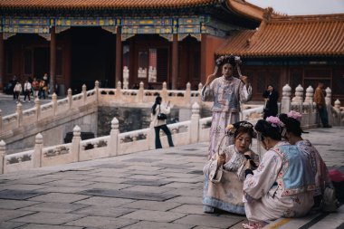 Pekin, Çin; 17 Ekim 2024: Yasak Şehir, Çin 'de geleneksel kostümler giyen bir grup Çinli genç kadın, birkaçı oturuyor ve telefonlarını kontrol ediyor.