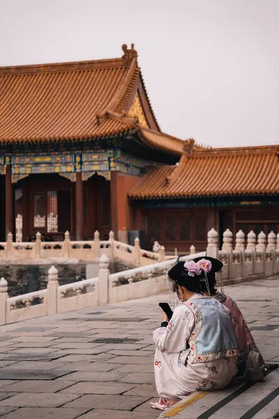 Geleneksel kostümler giyen ve Yasak Şehir, Çin 'de telefonlarını kontrol ederken oturan tanınmayan iki genç Çinli kadının arka plan görüntüsü.