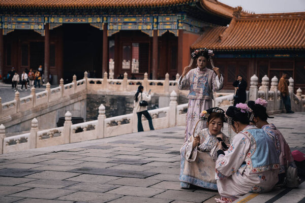 Пекин, Китай; 17 октября 2024 года: Группа китайских молодых женщин в традиционных костюмах в Запретном городе, Китай; некоторые из них сидят и проверяют телефон