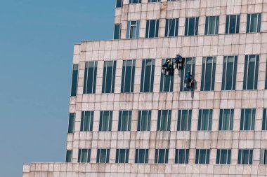 Cam siliciler parlak, güneşli bir gökyüzünün altında gökdelen cephesini özenle temizliyor, yeteneklerini ve takım çalışmalarını büyük yüksekliklerde sergiliyorlar. Bangkok, Tayland