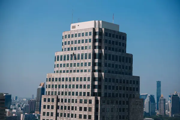 İplerden sarkan cam temizleyicileri Bangkok, Tayland 'daki modern bir gökdelenin camlarını temizliyor.