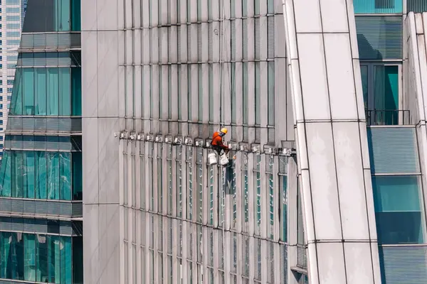 Yüksek katlı pencere temizleyicisi modern bir gökdelenin bakımını üstlenerek pırıl pırıl bir görünüm için pırıl temiz pencereler sağlıyor. Bangkok, Tayland