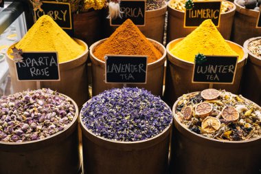 Çeşitli baharatlar, otlar ve çaylar yuvarlak ahşap kaplarda düzenli olarak düzenlenerek canlı renkler ve dokular sergileniyor; İstanbul baharat pazarı, Türkiye