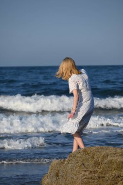 Hafif beyaz elbiseli romantik sarışın bayan sıcak ve güneşli bir günde sahil yürüyüşünün tadını çıkarıyor. İnanılmaz Kuzey Denizi 