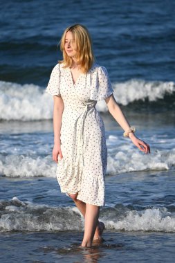 Hafif beyaz elbiseli romantik sarışın bayan sıcak ve güneşli bir günde sahil yürüyüşünün tadını çıkarıyor. İnanılmaz Kuzey Denizi 