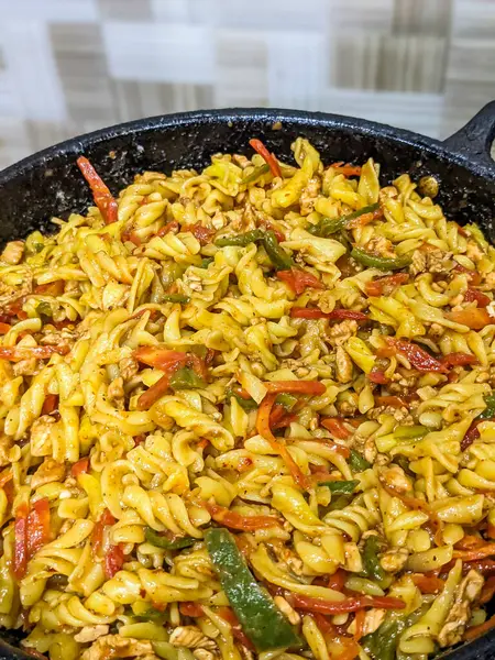 Tavada tavuk ve sebzeyle makarna pişirmek.