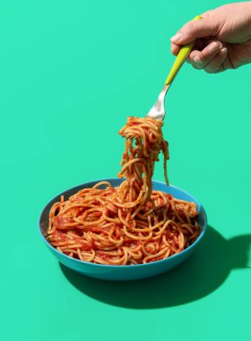 Kadının eli tabaktan çatallı spagetti alıyor. Klasik İtalyan yemeği, ev yapımı domates soslu makarna..