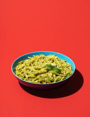 Klasik İtalyan yemeği makarnası, kırmızı masada Trofie al Pesto minimalisti. Pesto soslu makarna ve canlı renkli arka planda parmesan peyniri..