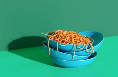 Tabakta Pomodoro makarnası yeşil renkli bir masada boş kaselerin üzerine istiflenmiş. Parlak ışıkta domates soslu spagetti..