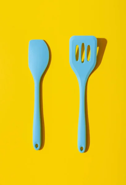 Above view with a set of blue kitchen utensils minimalist on a yellow table. Set of 2 blue spatulas isolated on a yellow-colored background