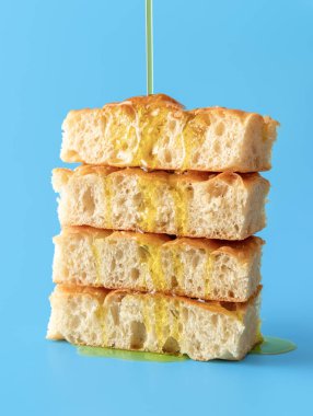 Focaccia ekmeğinin üzerine zeytinyağı dökmek, mavi bir masaya minimalist koymak. Zeytinyağı Focaccia dilimlerinin üzerine damlıyor..