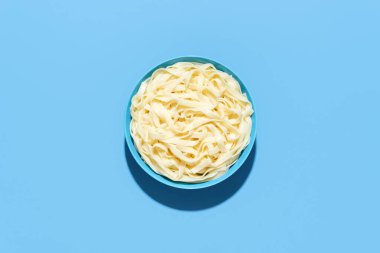 Üstünde bir kase tagliatelle makarnası, mavi bir masada minimalist. Renkli arka planda parlak ışıkta sossuz haşlanmış makarna.