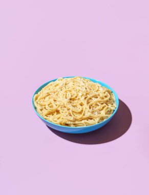 Klasik İtalyan yemeği, rendelenmiş parmesan ve karabiberli spagetti, mor bir masada minimalist. Makarna Cacio e Pepe mavi bir kasede renkli bir arka planda..