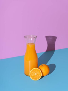 Freshly squized orange juice in a bottle, minimalist on a blue table. Carafe with orange juice in bright sun light on a colorful background.