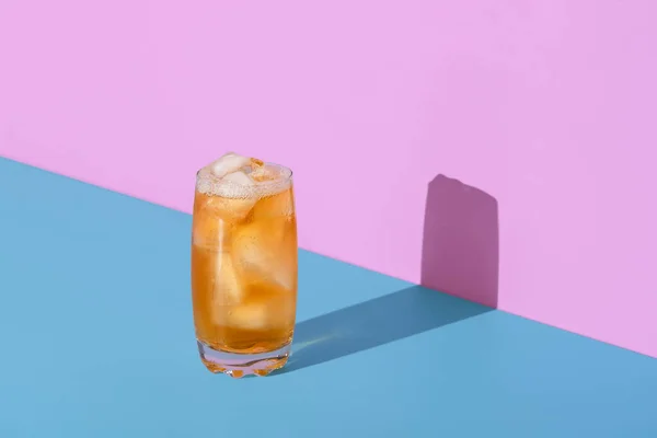 Glass with ice cubes and cold tea, minimalist on a blue table. Summer drink, ice tea, in bright light on a vibrant background.