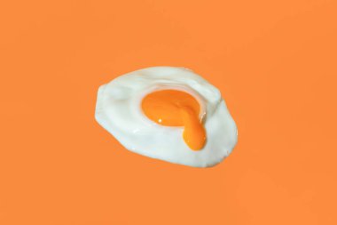 Close-up with a single sunny side up egg isolated on an orange background. Flying fried egg with the egg yolk drippin minimalist on a vibrant colored background.