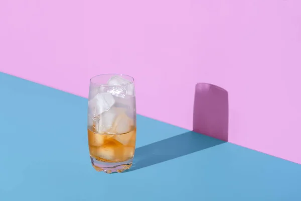 Glass with ice cubes and tea in bright light, minimalist on a blue table. A refreshing drink, iced tea in a frosty glass.