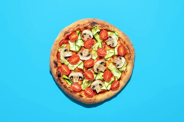 Top view with a homemade pizza minimalist on a blue table. Delicious vegan pizza with zucchini, tomatoes, and mushrooms.