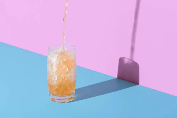 Pouring tea in a glass over the crushed ice, minimalist on a vibrant colored background. Glass with crushed ice and tea on a blue table in a bright light