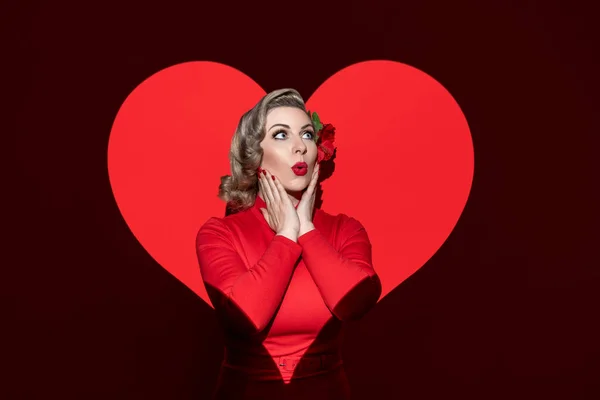 Portrait of a blonde woman with 50\'s characteristic hair, make-up, and clothes. A romantic concept with a retro-style woman isolated on a red background, with a heart-shaped light on her.
