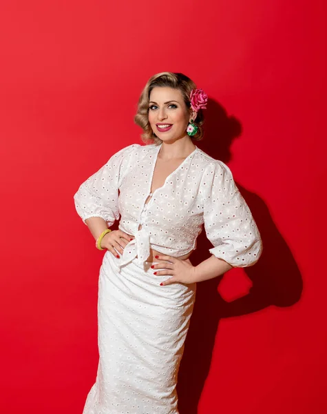 Blonde woman with a retro hairstyle in a white summer dress, minimalist on a red background. Beautiful smiling woman in bright light isolated on a vibrant colored background