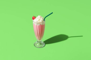 Yeşil bir masada tek bir bardak çilekli milkshake minimalistiyle yüksek açı manzarası. Çilek aromalı milkshake yeşil arka planda izole edilmiş.