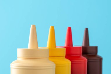 Plastik mayonez, ketçap, hardal ve barbekü sosu. Mavi arka planda sıralanmış çeşitli soslar.