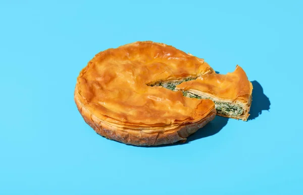 Homemade savory pie with spinach and cheese, balkan recipe, minimalist on a blue table. Delicious spinach cake made with phyllo dough