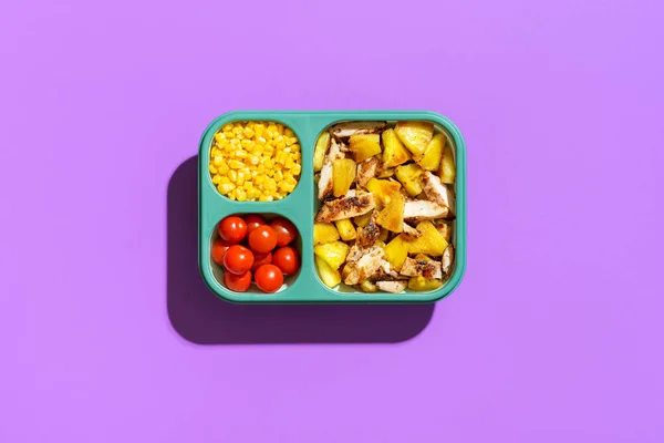 Top view with hawaiian chicken and pineapple salad in a lunch box, minimalist on a purple table. Sweet and sour dish, roasted pineapple and chicken meat, in a prep meal container.