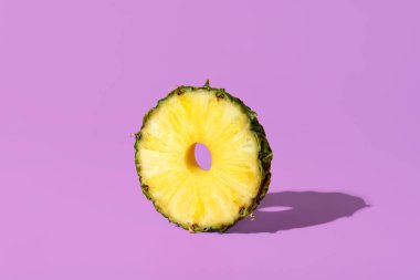 Mor bir masanın üzerinde parlak ışık minimalisti olan tek bir dilim ananas. Canlı bir arka planda izole edilmiş bir ananas meyvesi dilimi.