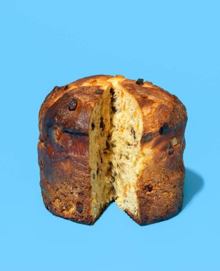 Mavi bir masanın üzerinde parlak ışık minimalisti dilimlenmiş panettone. Kuru üzümlü, şekerli portakal kabuklu ve çikolatalı ev yapımı ekşi ekmek tonu.