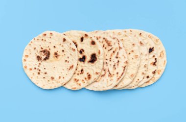 Yukarıda birkaç naan ekmeği, mavi bir masada minimalist. Ev yapımı düz Hint ekmeği, parlak ışık altında, canlı bir arka planda izole edilmiş.