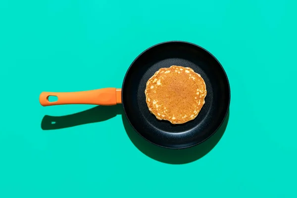 Above view with a pancake in a pan, minimalist on a green table. Homemade pancake in an iron cast pan, in bright light, isolated on a vibrant background
