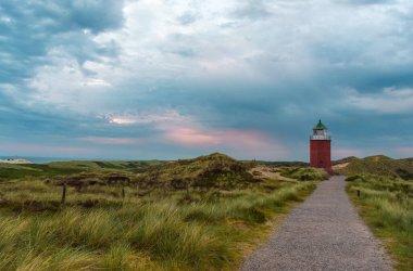 Kuzey Denizi, Almanya 'da, Sylt adasında yağmurlu bir günde gün batımı manzarası. Akşam doğa manzarası bulutlu bir gökyüzü ve yeşil marram otuyla