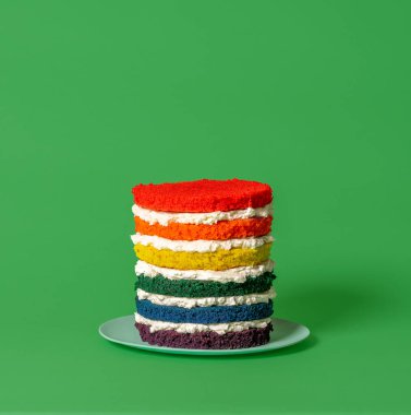 Gökkuşağı rengi hamurlu çok katmanlı kremalı pasta, yeşil arka planda minimalist