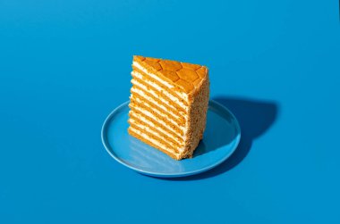 Bir dilim medovik, bal katmanlı kek, mavi arka planda izole edilmiş.