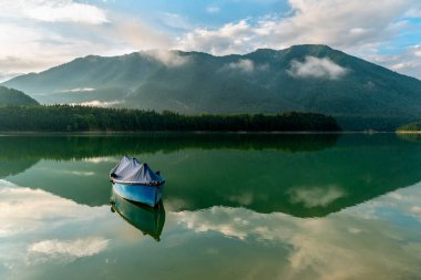 Sylvenstein Gölü 'nde yüzen tek bir tekne ve suda Bavyera Alpleri' nin yansıması olan manzara.