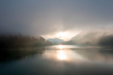 Gündoğumunda Sylvenstein Gölü 'nün sisli ve arka planda dağların silueti olan hava manzarası.