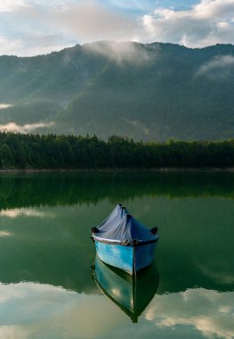 Sylvenstein Gölü 'nde yüzen tek bir tekne ve suda Bavyera Alpleri' nin yansıması olan manzara.