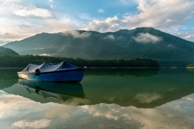 Sylvenstein Gölü 'nde yüzen tek bir tekne ve suda Bavyera Alpleri' nin yansıması olan manzara.
