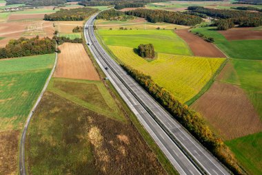 Sonbahar ormanı ve tarım alanlarından geçen iki şeritli bir Alman otoyolunun insansız hava aracı görüntüsü.