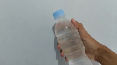 Mavi arka planda plastik bir şişede soğuk su bulunduruyor..