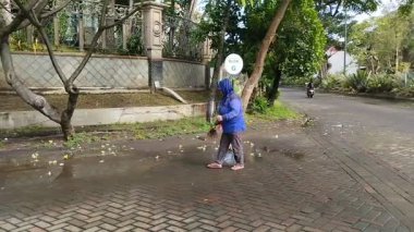 Surabaya, Endonezya - 18 Mayıs 2025: Evin önündeki düşen çiçekleri süpüren bir hademe