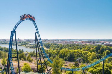 Helsinki, Finlandiya - 24 Haziran 2022: Hız treni Taiga ile Linnanmaki eğlence parkının en üst görüntüsü bulanık hareket ve Helsinki kenti.