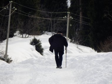 Almaty, Kazakhstan - March 6 2017: An old man with a stick walks to his home in the mountains outside Almaty. clipart